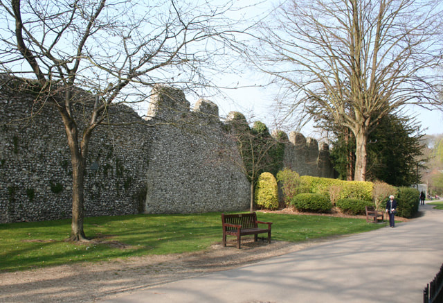 Photograph of the medieval walls of Winchester with two leafless trees and a bench