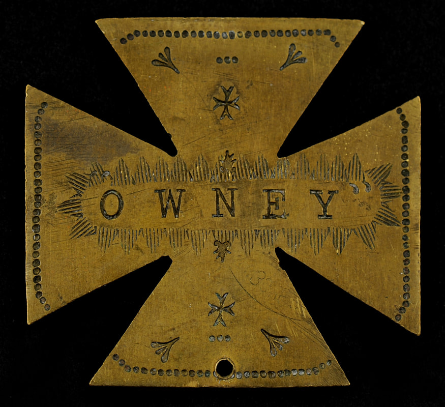 Metal tag shaped like a Maltese cross with Owney written across the middle