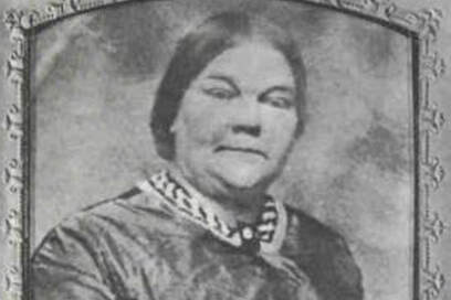 Black and white image of a middle aged woman with dark hair pulled back severely